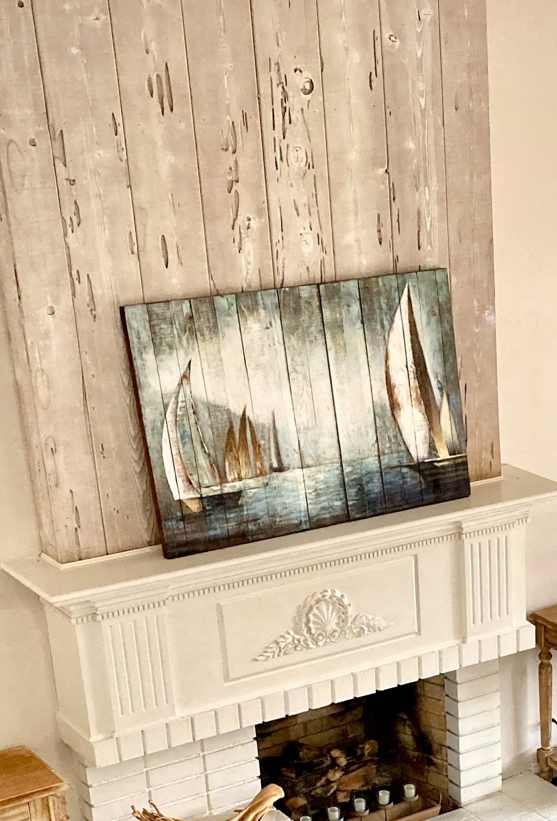 Detail of a white fireplace mantel with a hand-painted sailboat artwork against a reclaimed wood accent wall